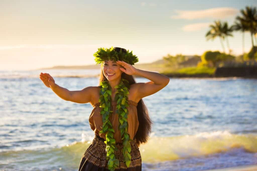 A smiling hula dancer adorned with a lei and traditional attire on a Hawaiian beach, showcasing the cultural beauty for babymoon visitors