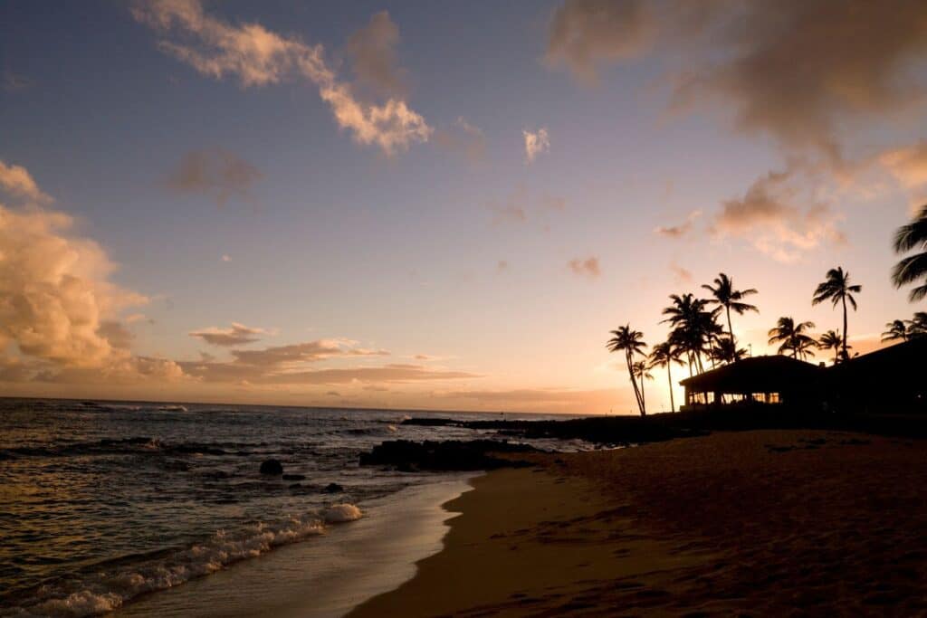 A golden sunset in Kaui with calm waves breaking on a golden sandy beach