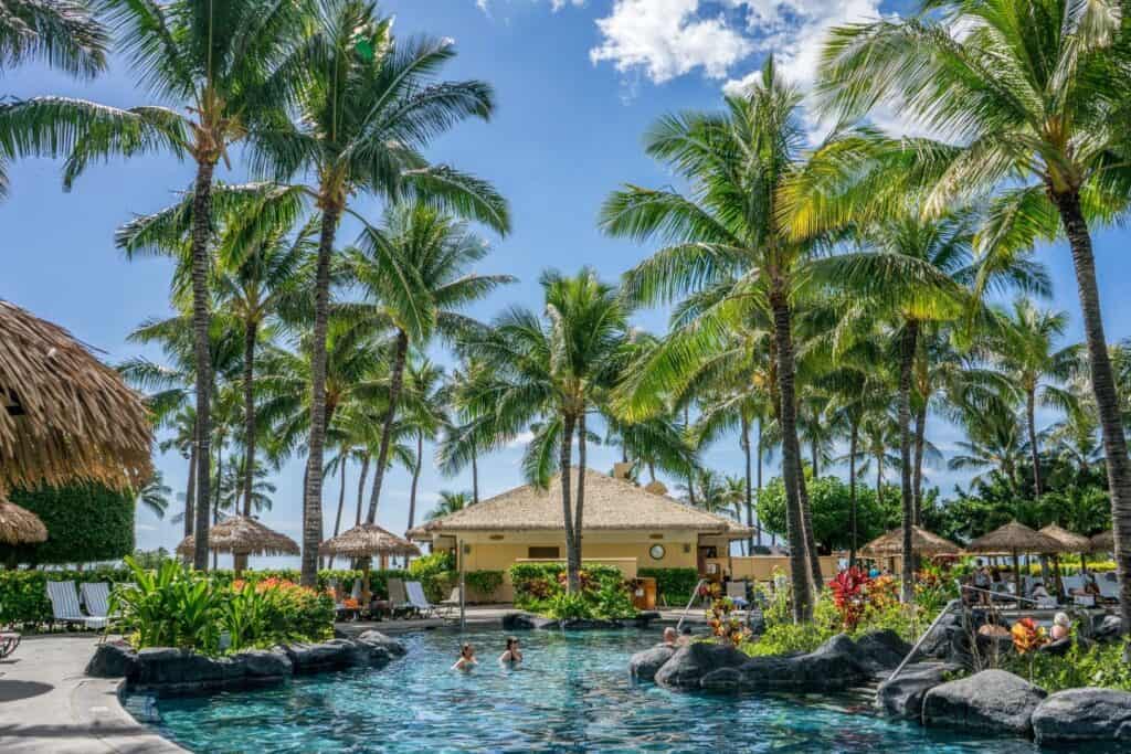 A serene resort pool surrounded by palm trees in Hawaii, an ideal relaxation spot for parents-to-be on a babymoon.