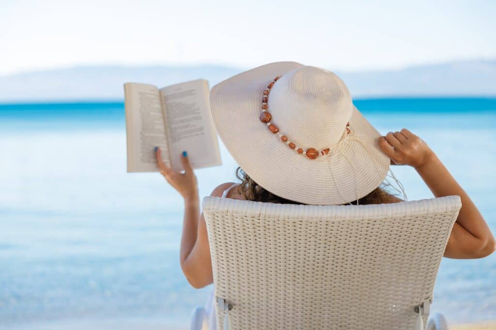 Relaxed woman reading a book on a beach chair by the sea, enjoying the peaceful solitude one might seek during a babymoon in the Florida Keys