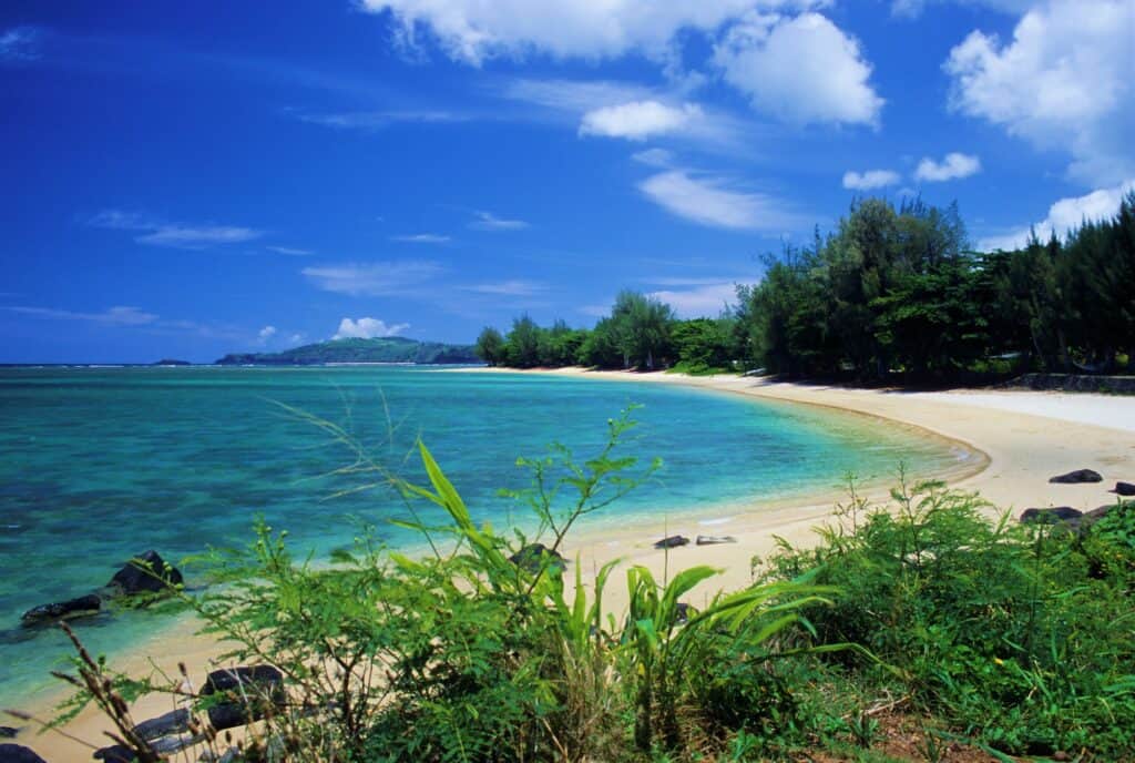 A serenie and clam beach at Anini Beach in Kauai with bright blue skies above and very few clouds. The perfect escape for your babymoon