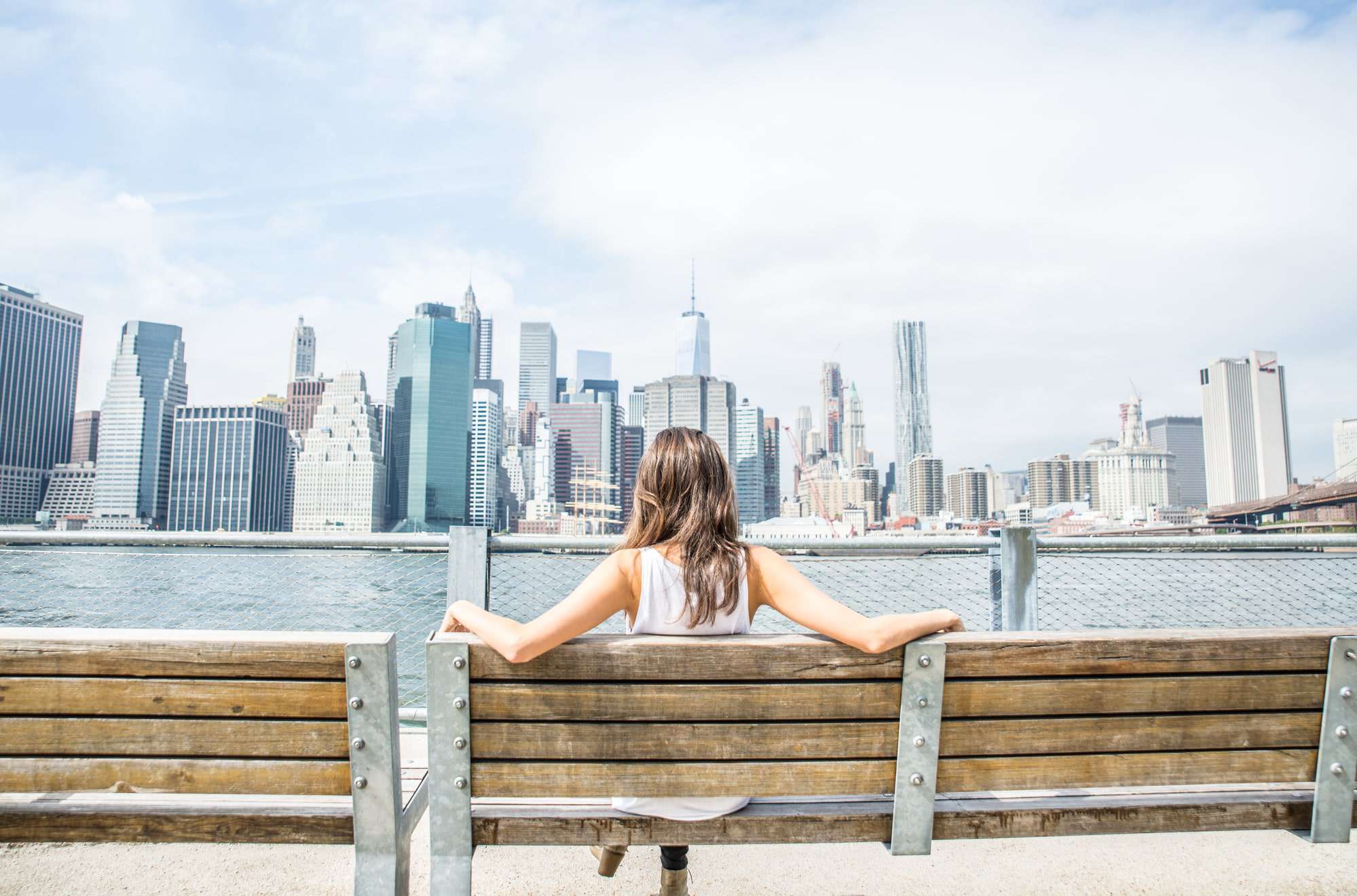 Woman sitting on a bench on a sunny day in New York looking at the city skyscrapers