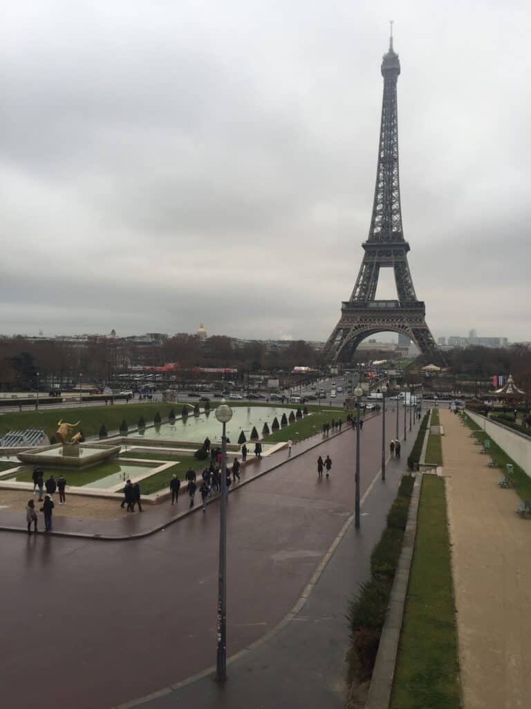 The Effile Tower on a dark cloud rainy day with a few people in the park in front of it.