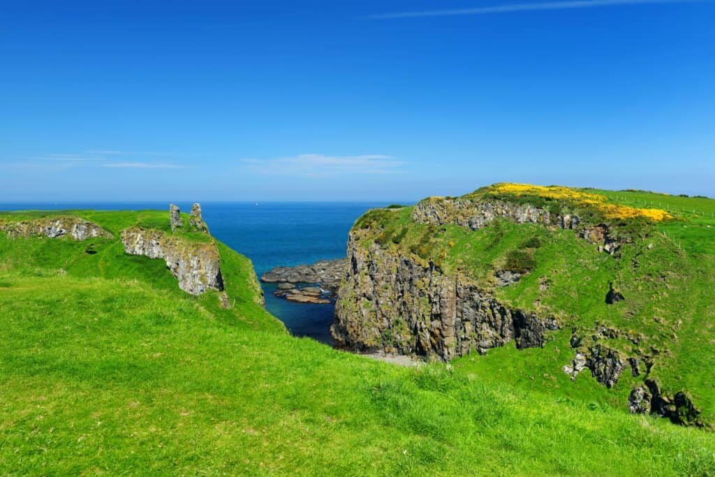 Bright green cliffs and mountains on the coast in Ireland with bright blue skies and ocean in the background