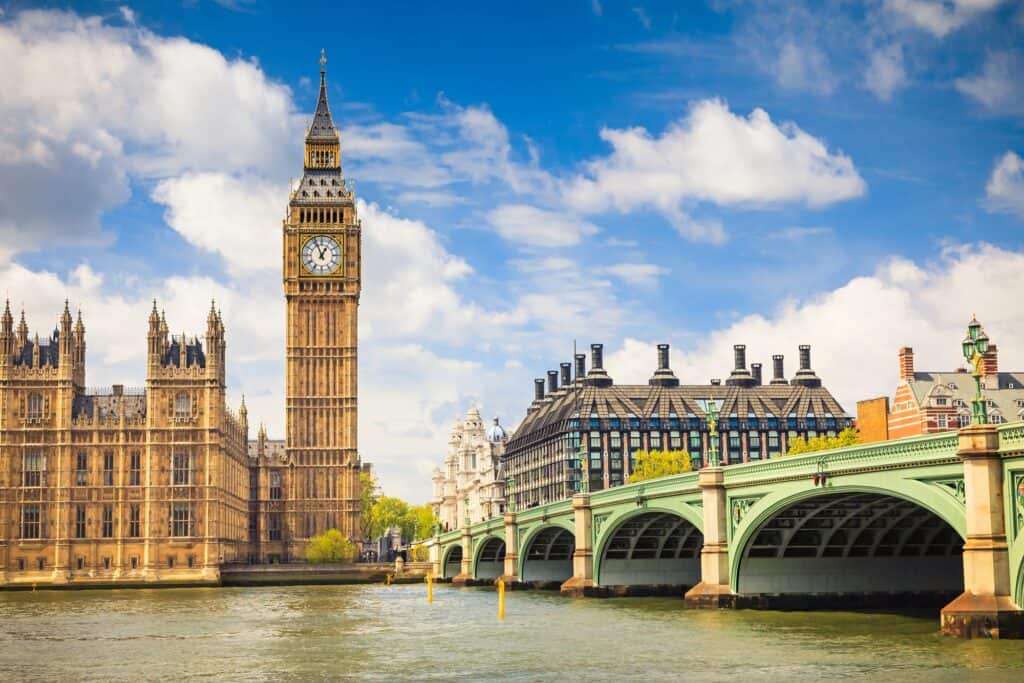 Big ben and a river with a green bridge on a semi cloudy day with blue skies in London
