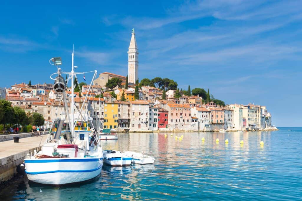 A small sail boat parked infront of a coastal city in Coatia with bright blue skies