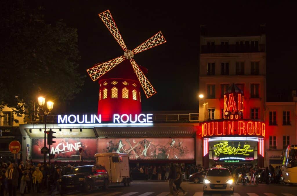 Moulin Rouge lite up at night with neon signs and a windmill on top